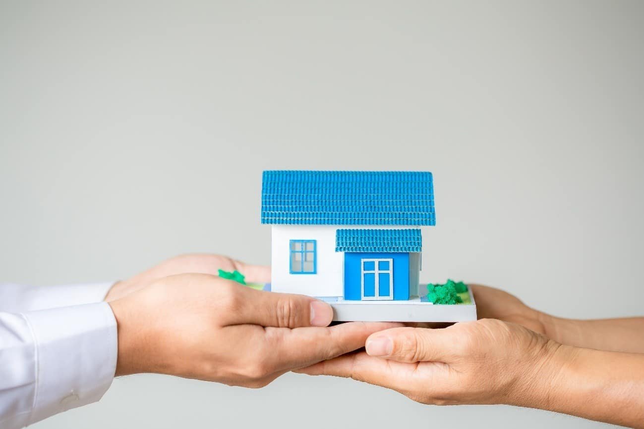 Mãos entregam a miniatura de uma casa a outra pessoa