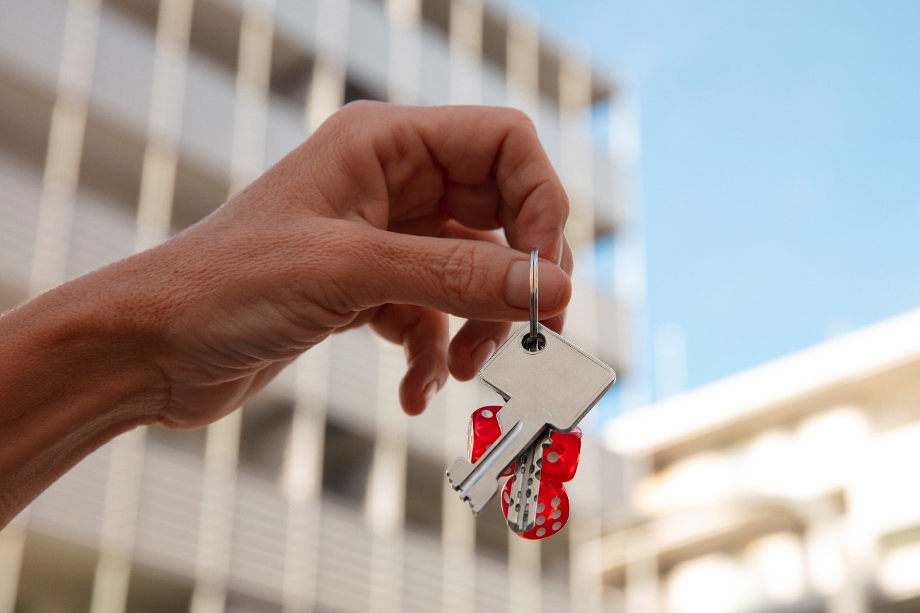 Mão segura as chaves de um apartamento diante de um prédio residencial